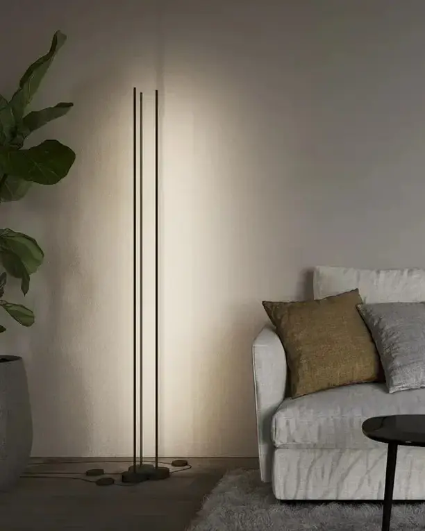 Een vloerlamp van drie dunne zwarte staven naast een grijze bank