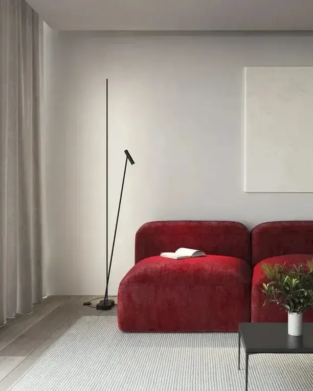 Een slanke zwarte vloerlamp naast een rode bank in een lichte kamer