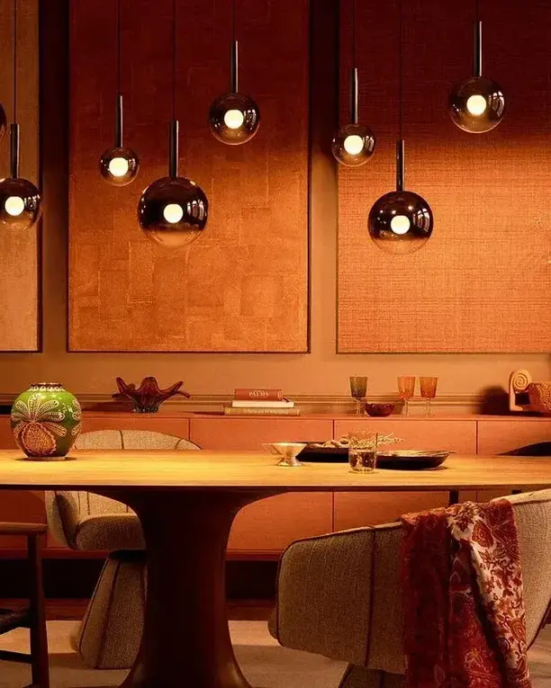 Glazen Luna-hanglampen op verschillende hoogtes boven een ovale houten eettafel, bij avond