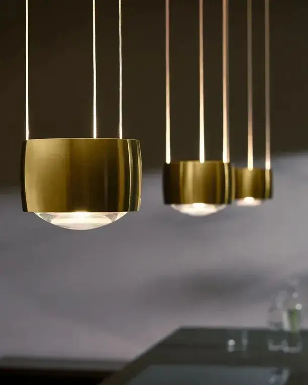 Messing lampkoppen op verschillende hoogtes boven een blad, met de schaduw van bladeren op de wand