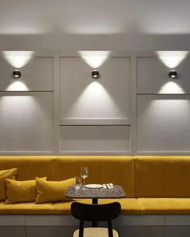 Een rij wandlampen met licht naar boven en beneden boven een okergele bank in een restaurant