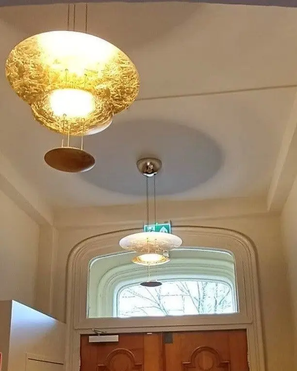 Twee hanglampen met bladgoud in een hal met een boogvormig raam boven de voordeur