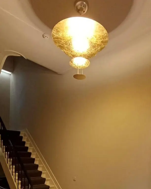 Een goudkleurige hanglamp boven een trap met een marmeren vloer