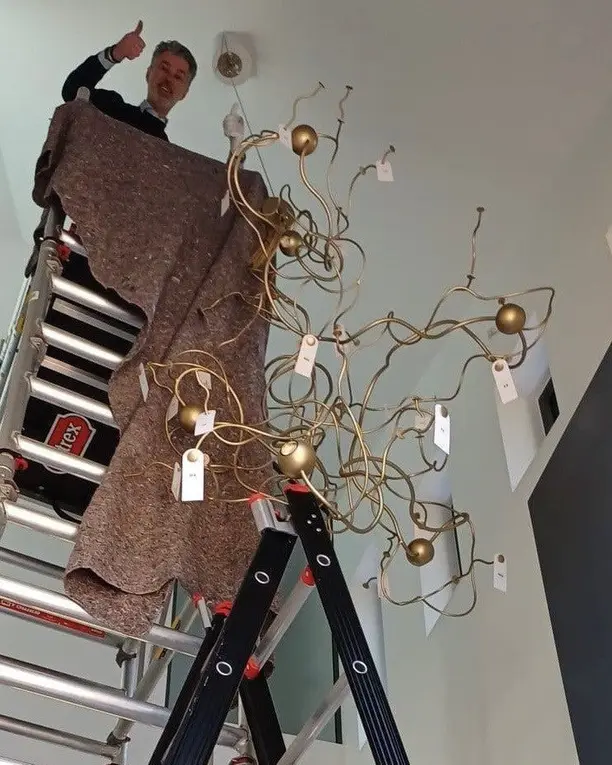 Een monteur bovenop een rolsteiger hangt de kroonluchter op, afgedekt met een deken