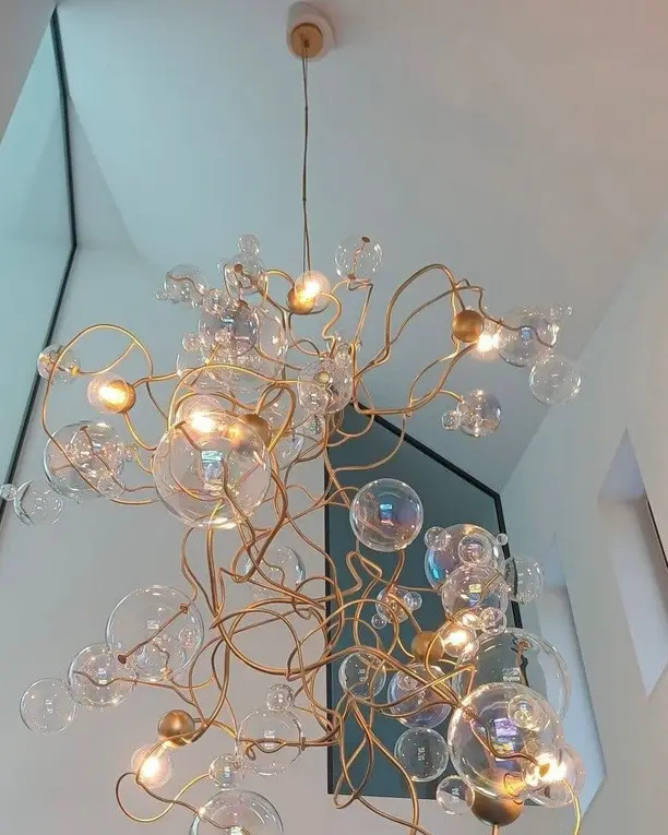 De kroonluchter met gouden takken en glazen bollen hangt in een hoog wit trappenhuis