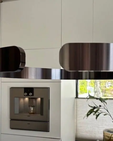 Twee geborstelde ringlampen boven een witte keuken met een ingebouwde koffiemachine