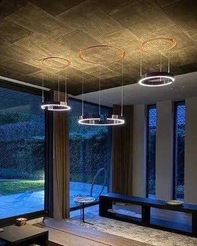 Drie ringvormige hanglampen boven een zithoek, met hoge ramen en een terras in de schemering
