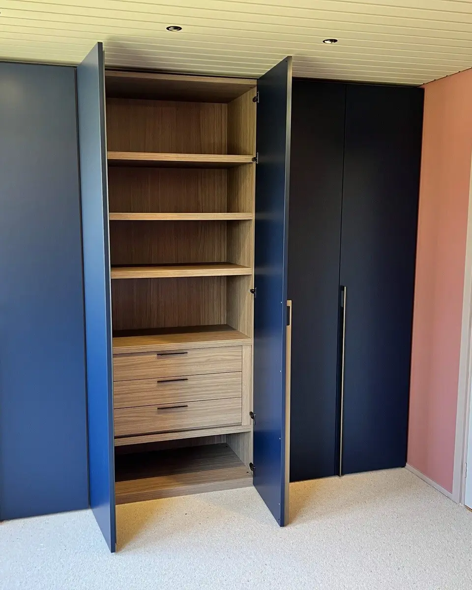Een donkerblauwe kledingkast op maat met open deuren: houten planken en drie laden achter de deuren
