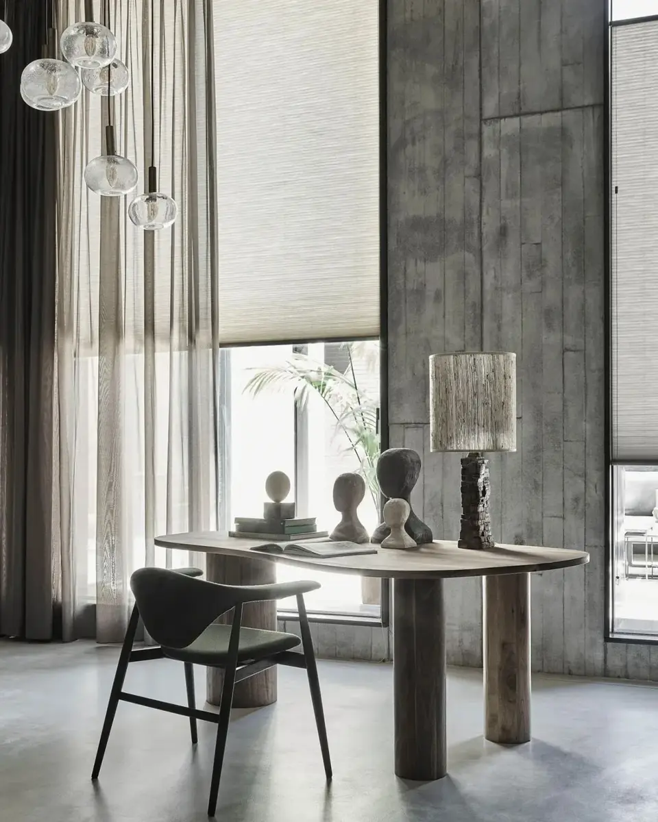 Hoge ramen met plissé en transparante gordijnen tegen een betonwand, glazen hanglampen boven een ronde tafel