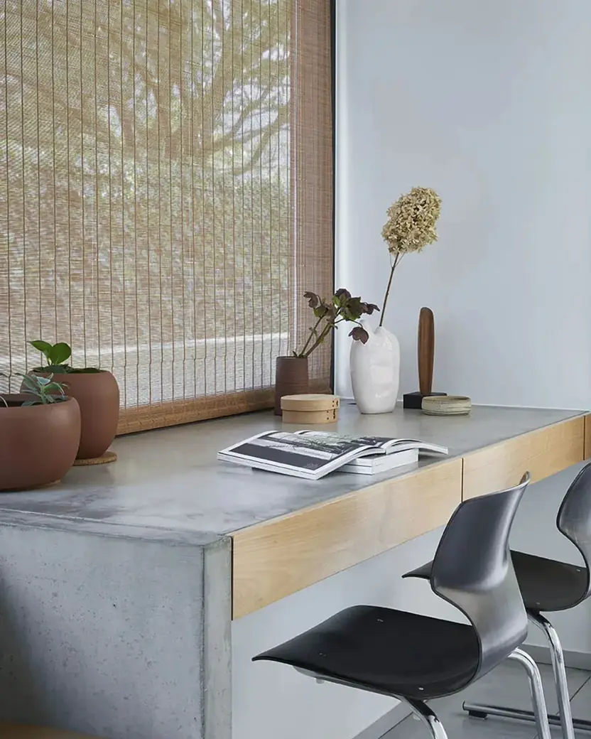 Geweven rolgordijn boven een bureau van beton en eiken, met terracotta potten