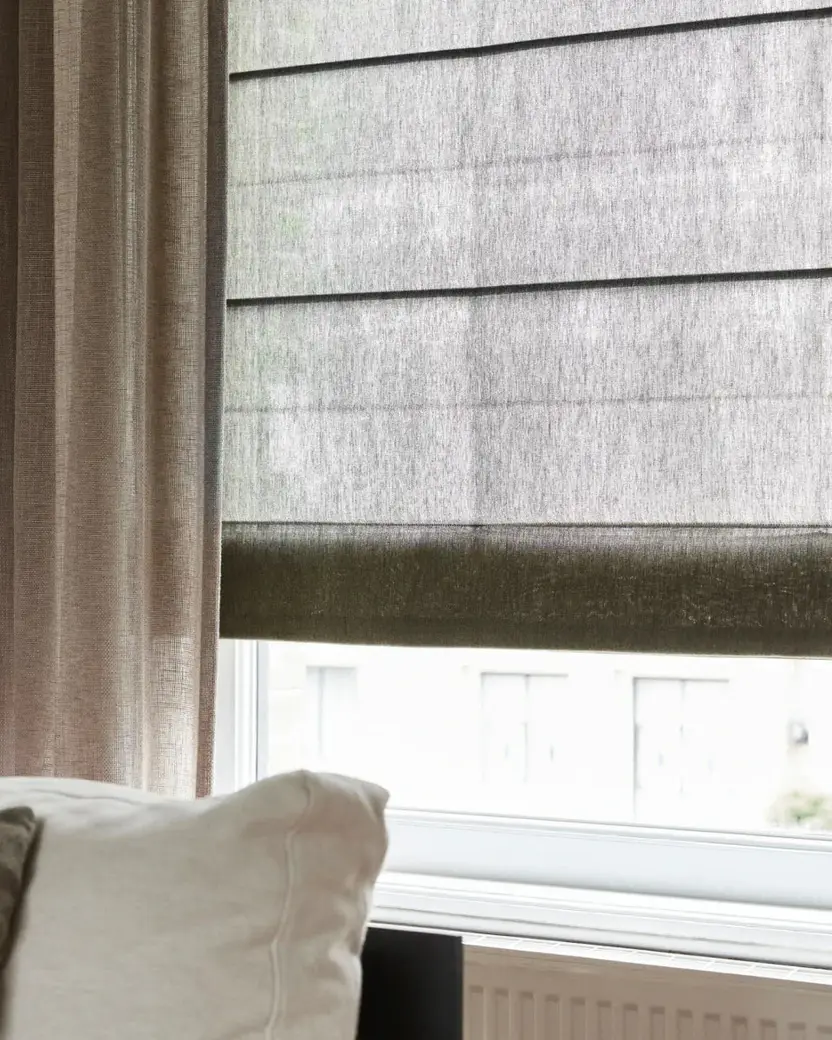 Donker linnen vouwgordijn, half opgetrokken, naast een taupe gordijn
