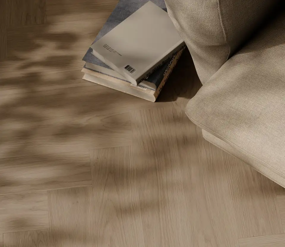 Lichte eiken visgraatvloer van bovenaf met bladschaduw, een stapel boeken en de hoek van een linnen bank