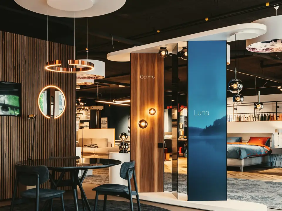 De Occhio-hoek in onze showroom: een lichtring boven een ronde tafel, en een zuil met het Occhio-woordmerk, twee bolvormige wandlampen en een blauwe Luna-banier