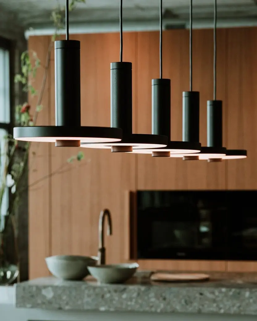 Vijf zwarte hanglampen op een rij boven een kookeiland van terrazzo, voor een houten wand
