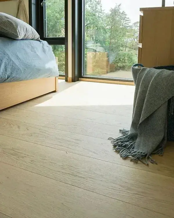 Een zolderslaapkamer met een lichte eiken vloer, een bed en een grote raampartij