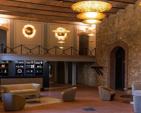 Een hotellounge met natuurstenen muren, een balkenplafond en getrapte hanglampen met bladgoud boven lage fauteuils