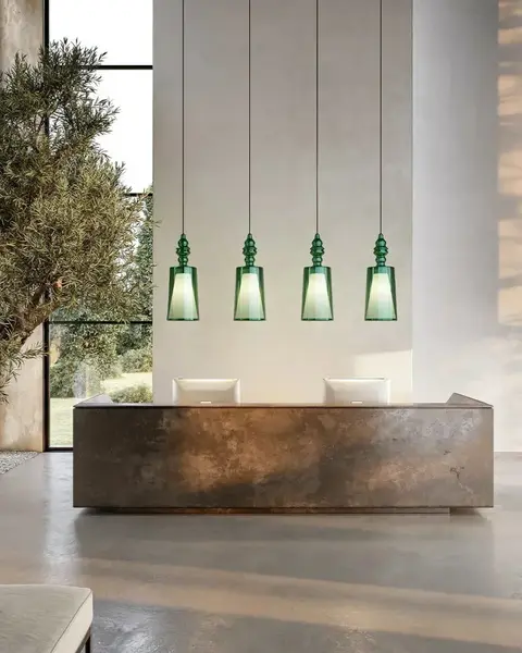 Een stenen balie onder vier groene glazen hanglampen, met een olijfboom en hoge ramen