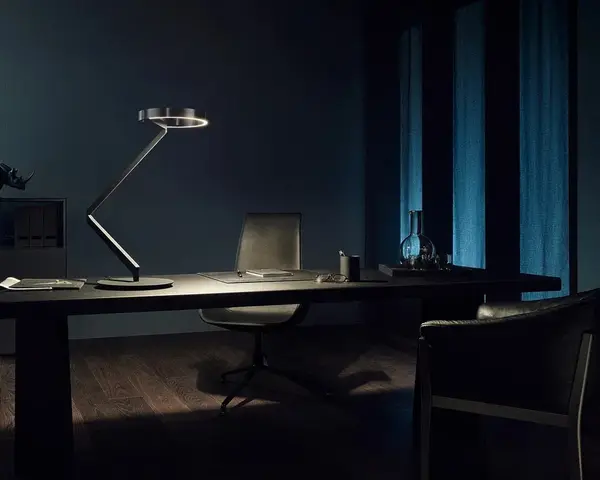 Een zwarte bureaulamp op een donker bureau met een leren stoel, in een kantoor met blauwe gordijnen bij avond